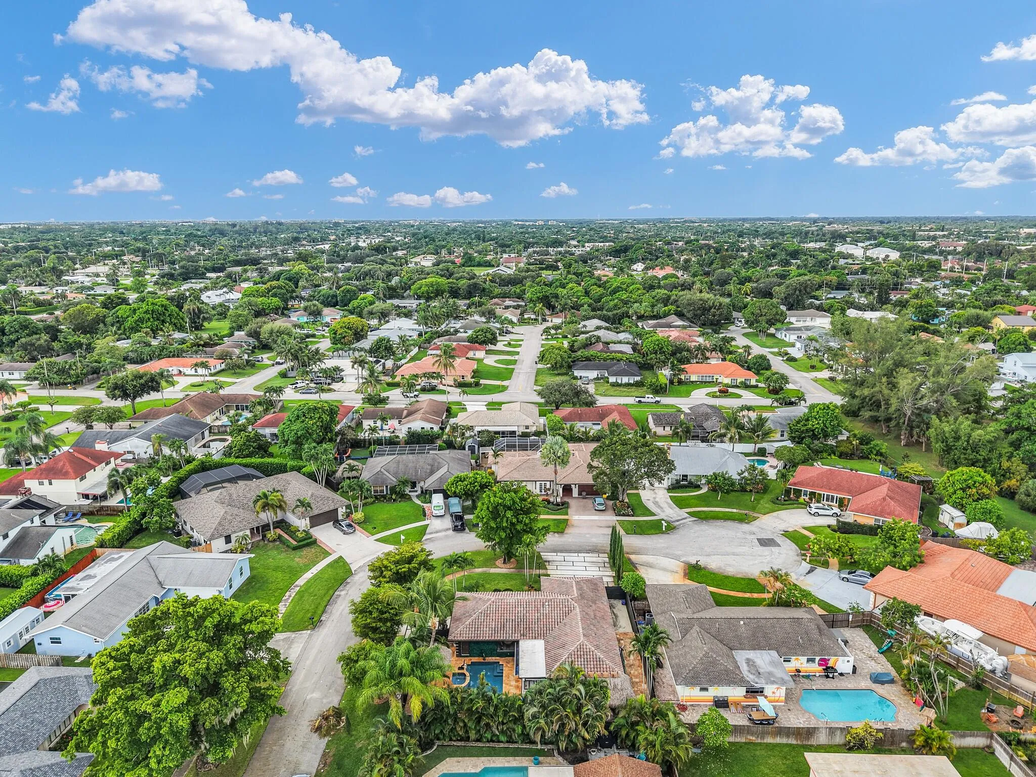 Aerial perspective showcasing a residential neighborhood with mature landscaping and multiple properties featuring private swimming pools