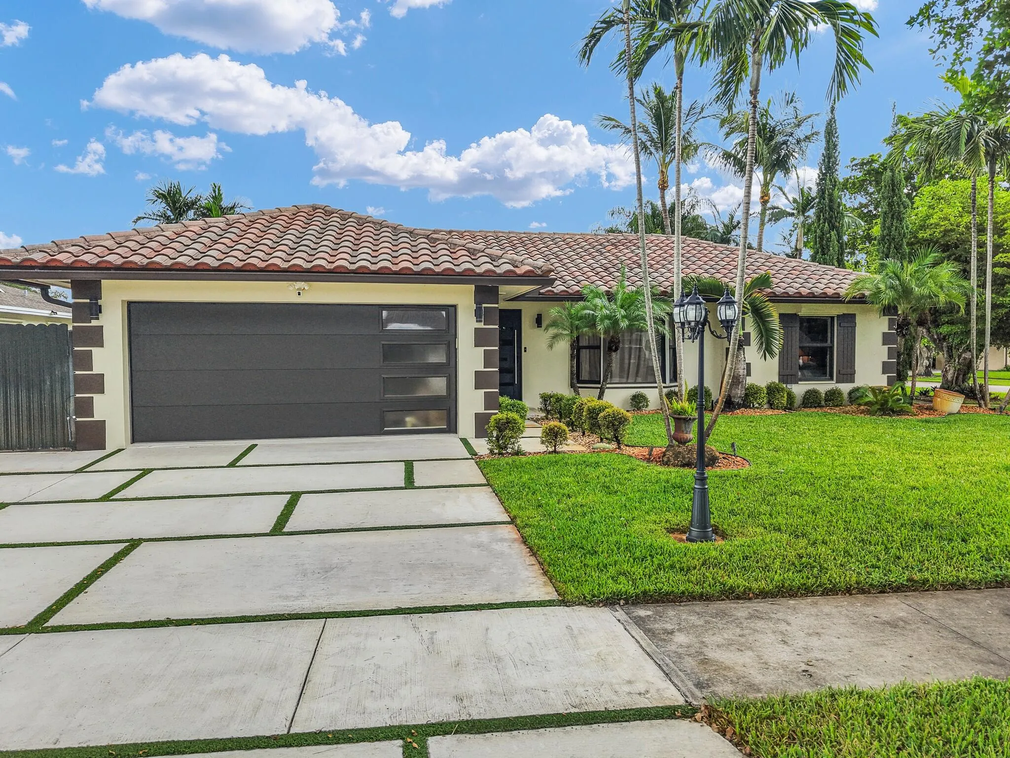 Exterior featuring a tile roof, stucco finish, a contemporary garage door with frosted panels, a concrete paver driveway with turf accents, and established landscaping