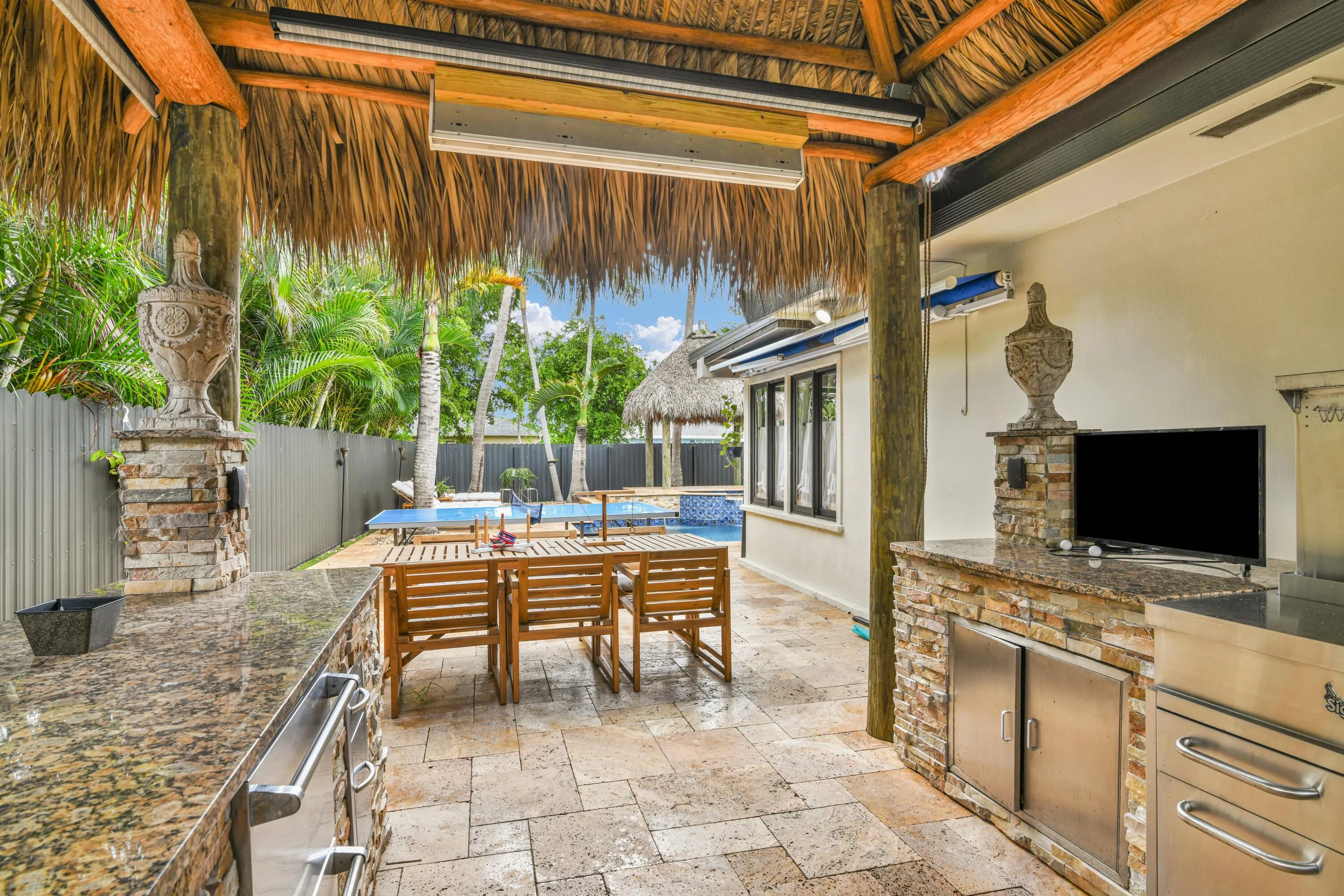 Thatch-roof covered patio featuring a built-in outdoor kitchen with stone veneer and granite countertops