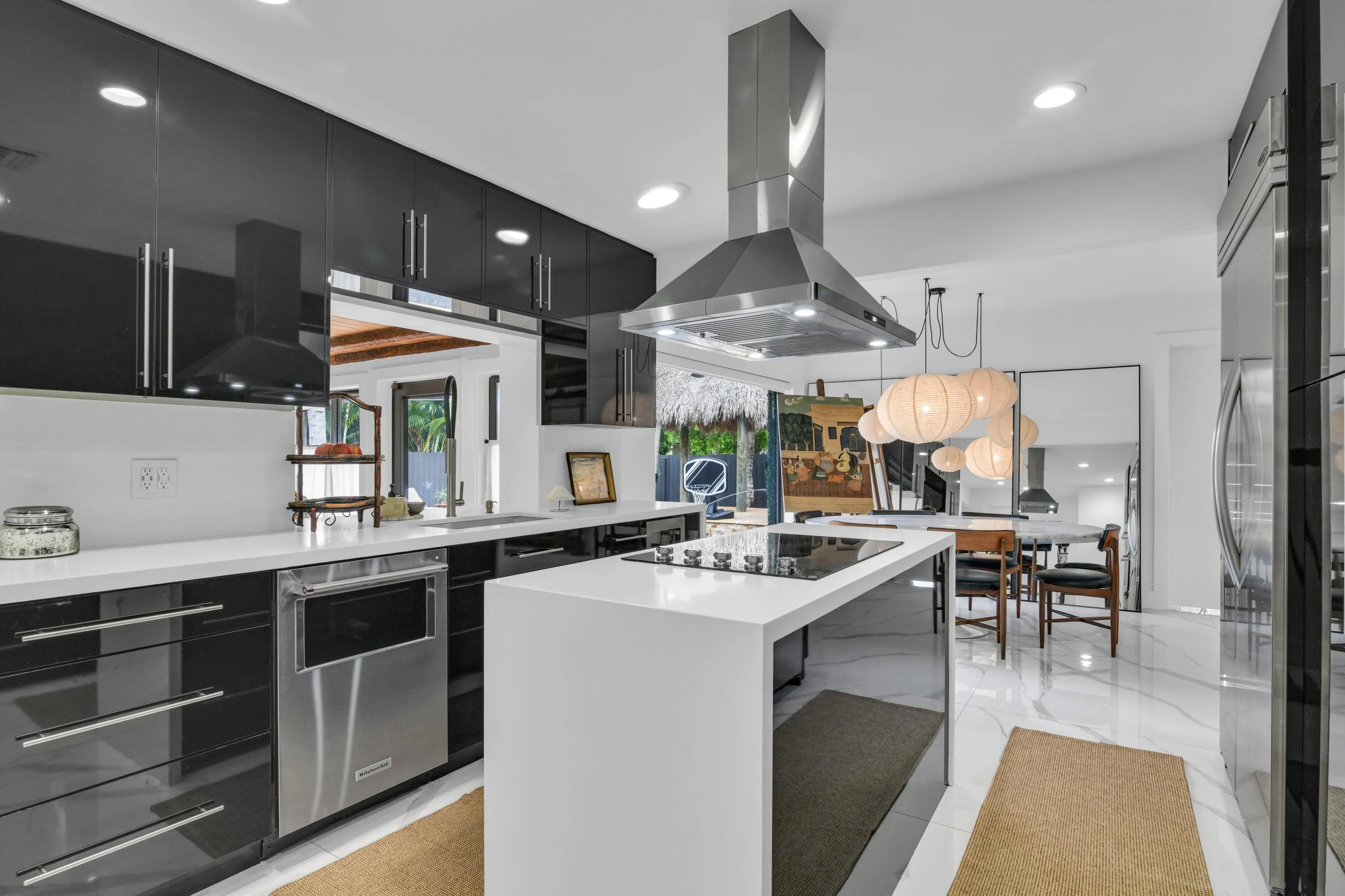 Modern kitchen featuring high-gloss black cabinetry, white countertops, stainless steel appliances, and an island with a built-in cooktop