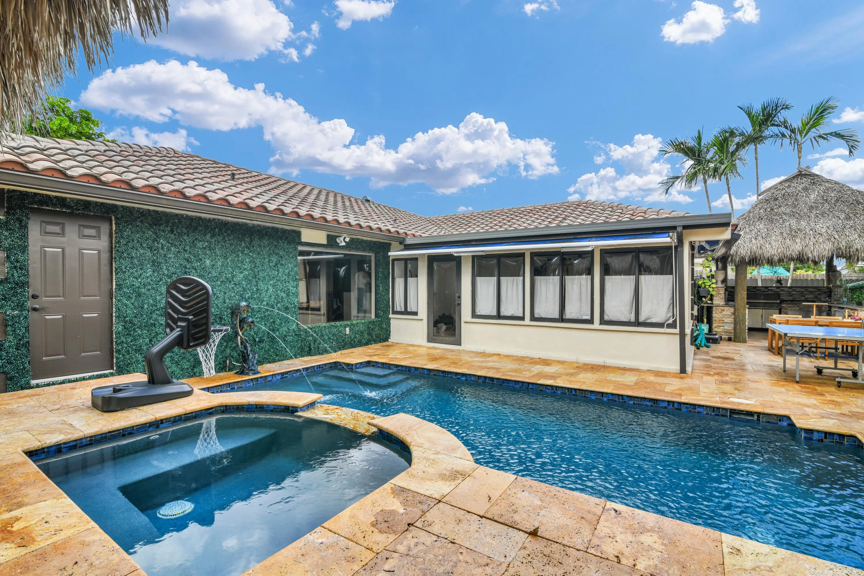 Swimming pool with integrated spa, surrounding stone-tile patio, covered outdoor structure, and tiled roofline