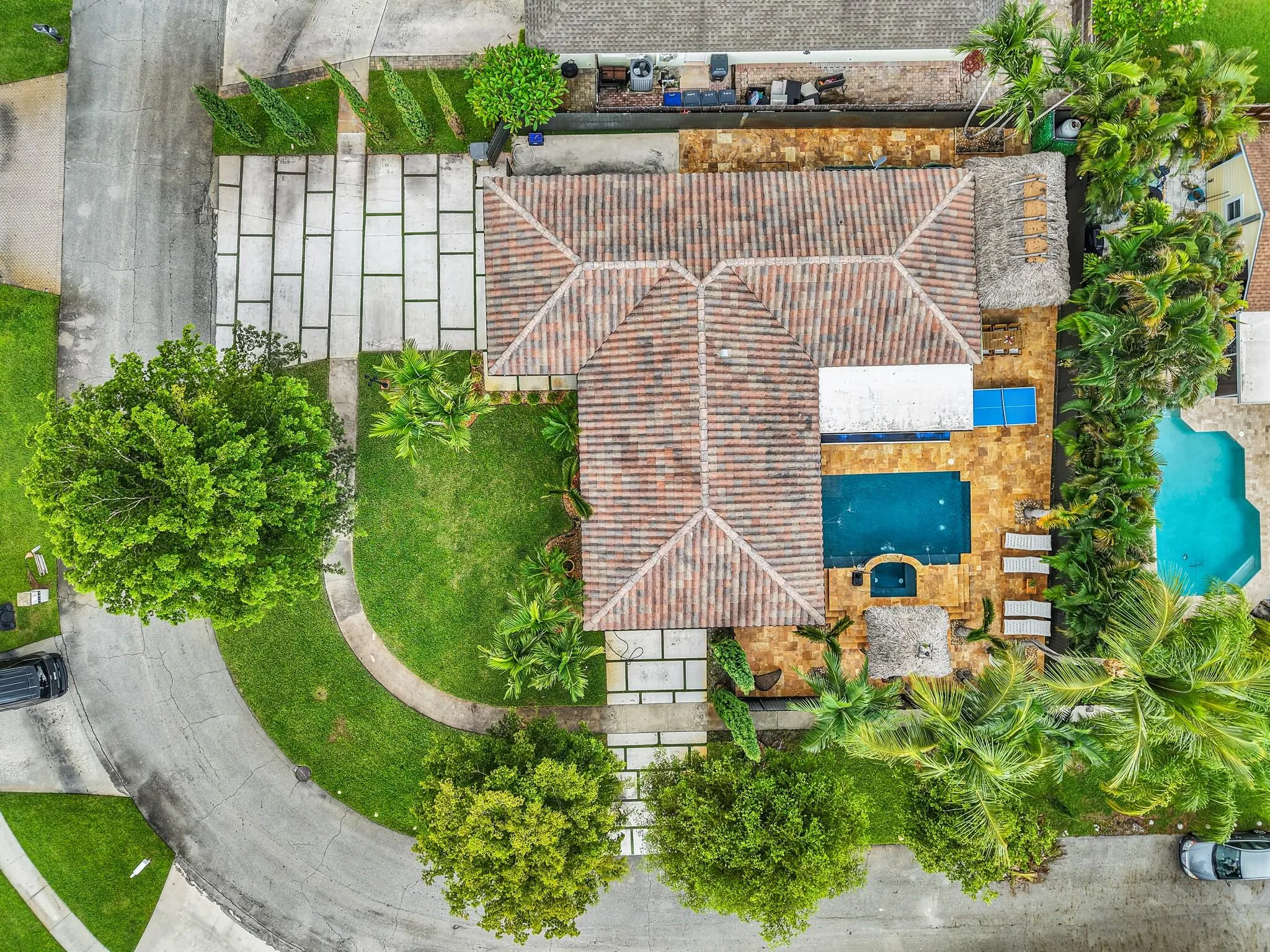Terracotta tile roof with a geometric paver driveway, featuring a private swimming pool, spa, and thatched-roof gazebo
