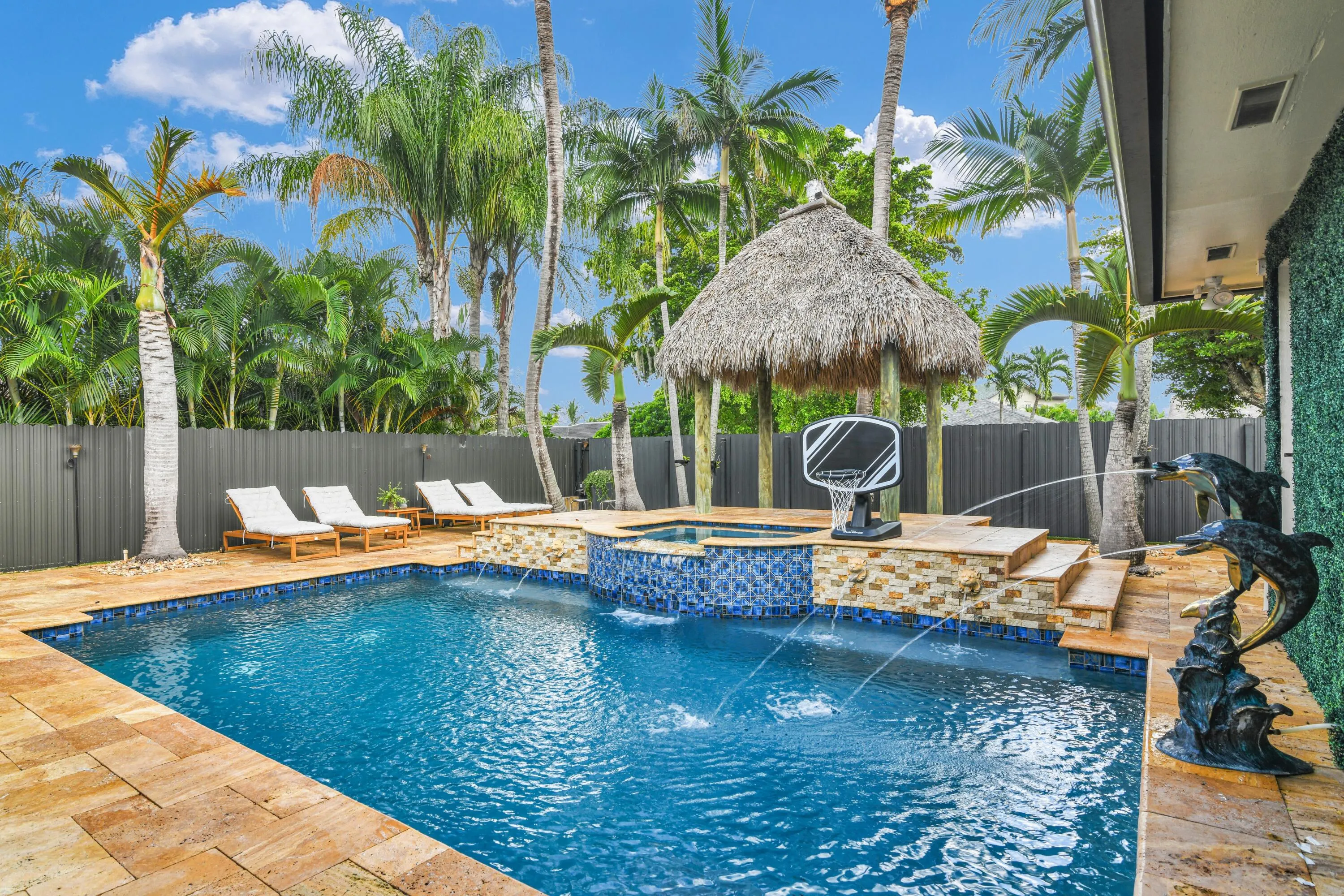 Pool deck with stone pavers, a tiled spa, a thatched-roof cabana, and a privacy fence