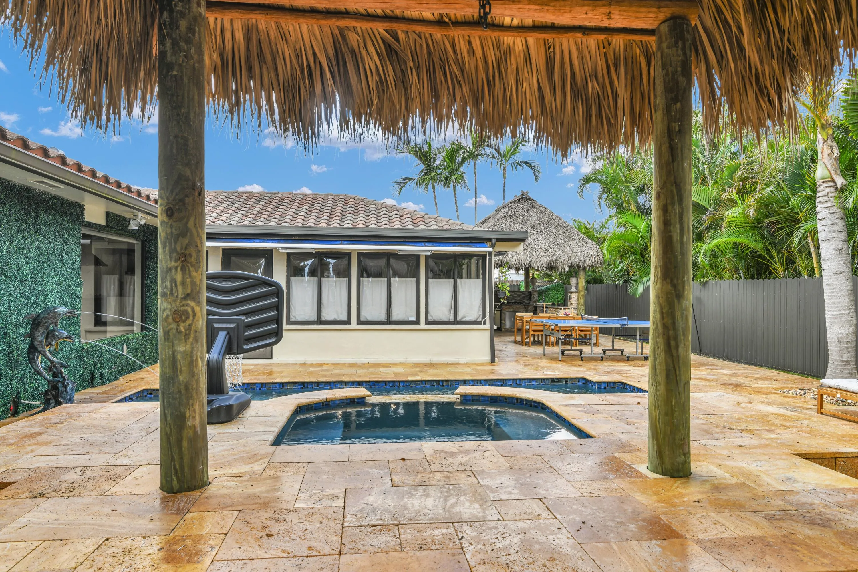 Expansive patio with stone tile flooring, a built-in pool, and a thatched-roof cabana