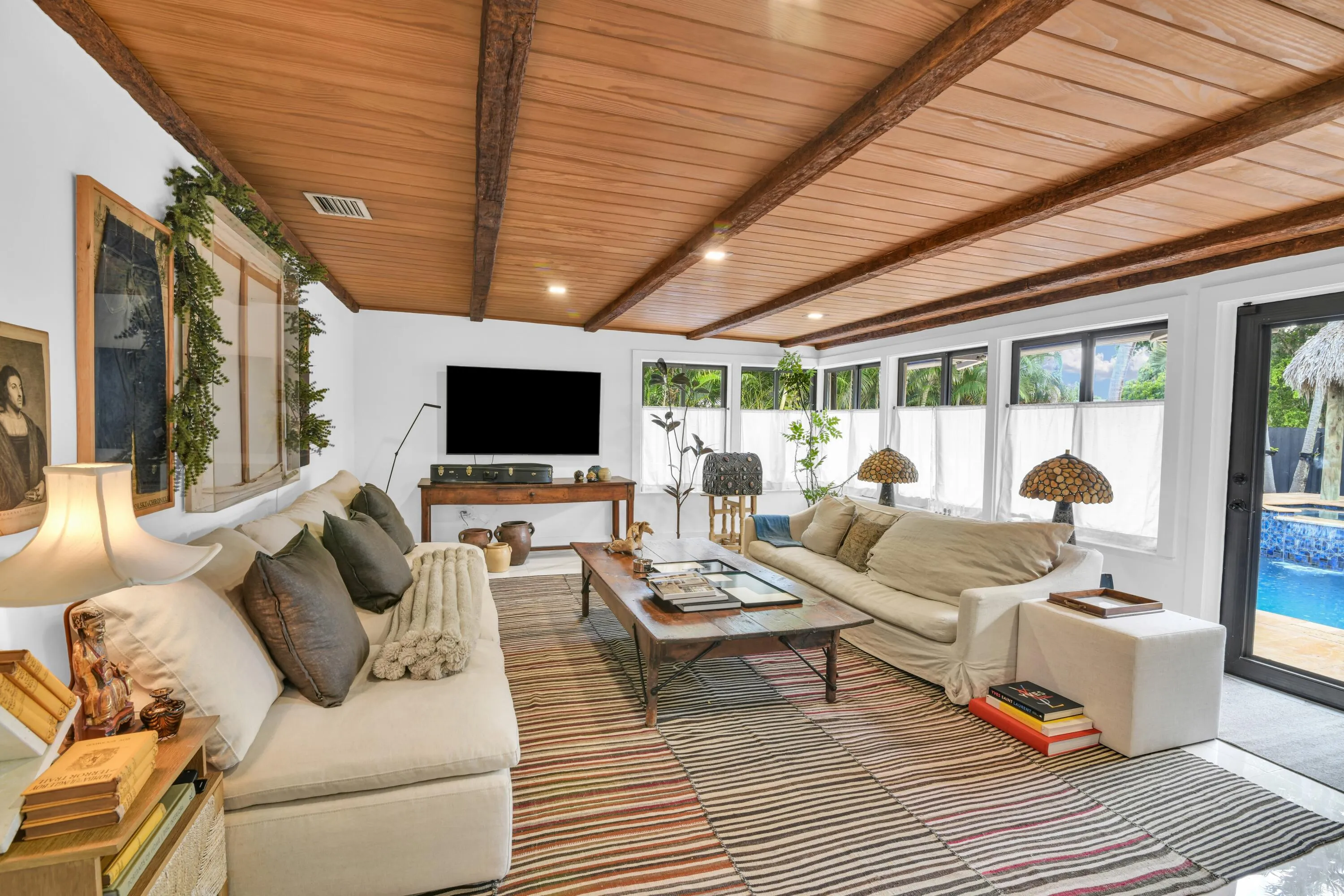 Wood-paneled ceiling with exposed beams, recessed lighting, multiple windows, and a glass-paneled door opening to a pool area
