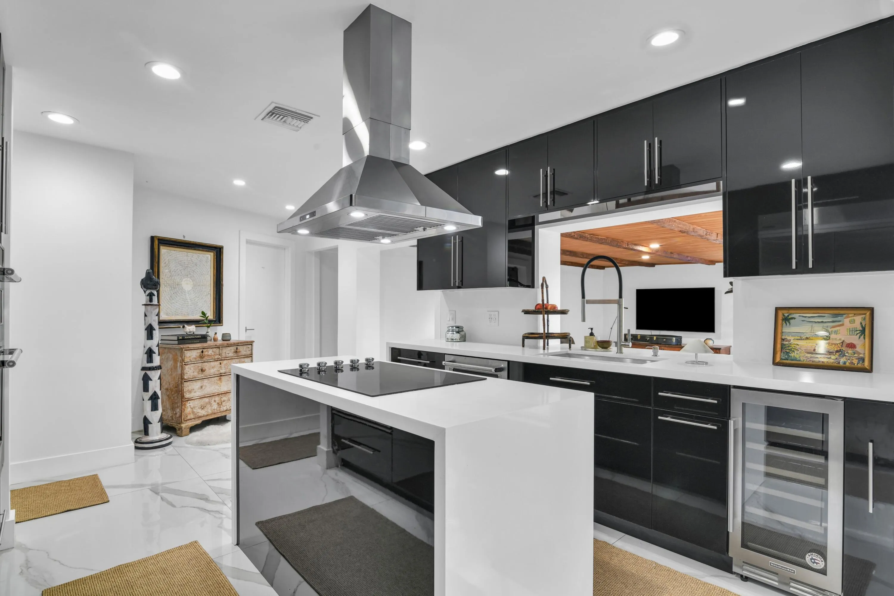 Kitchen featuring a center island cooktop, stainless steel range hood, white countertops, black cabinetry, and a built-in beverage cooler