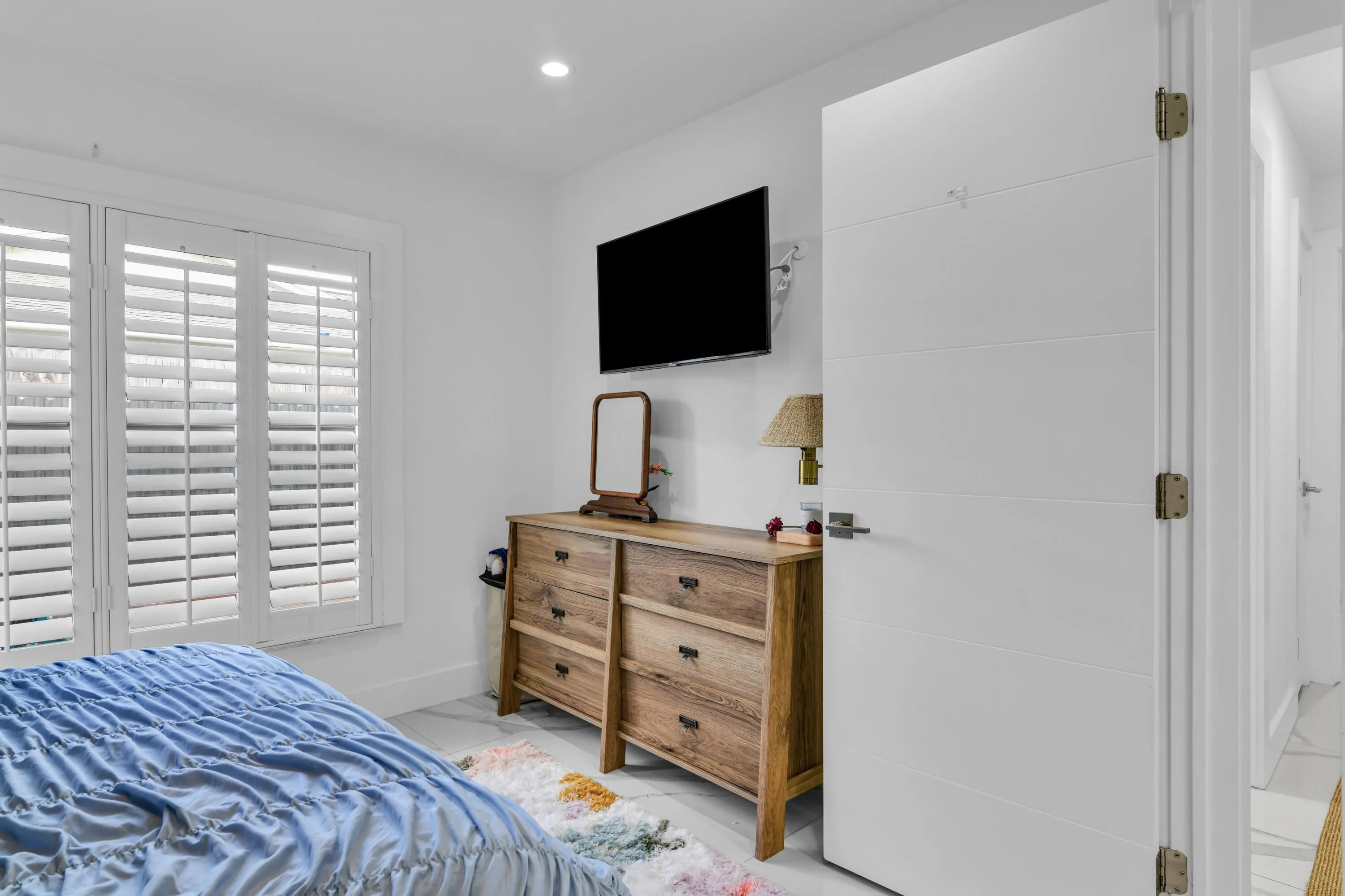 Plantation shutters, recessed ceiling lighting, wall-mounted television, and a flat-panel interior door
