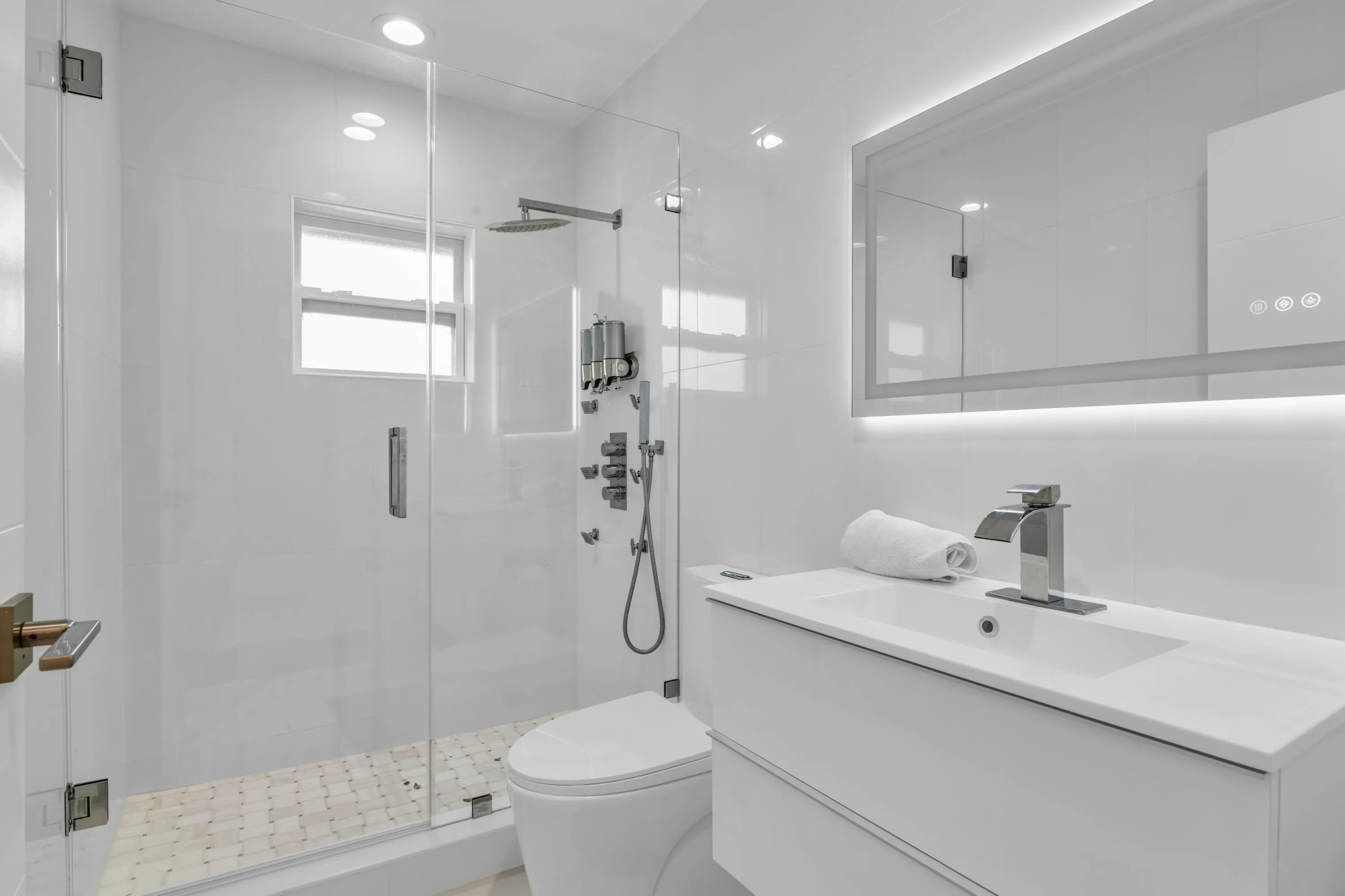 Modern bathroom featuring a frameless glass shower enclosure, a wall-mounted vanity with integrated sink, and an illuminated mirrored medicine cabinet