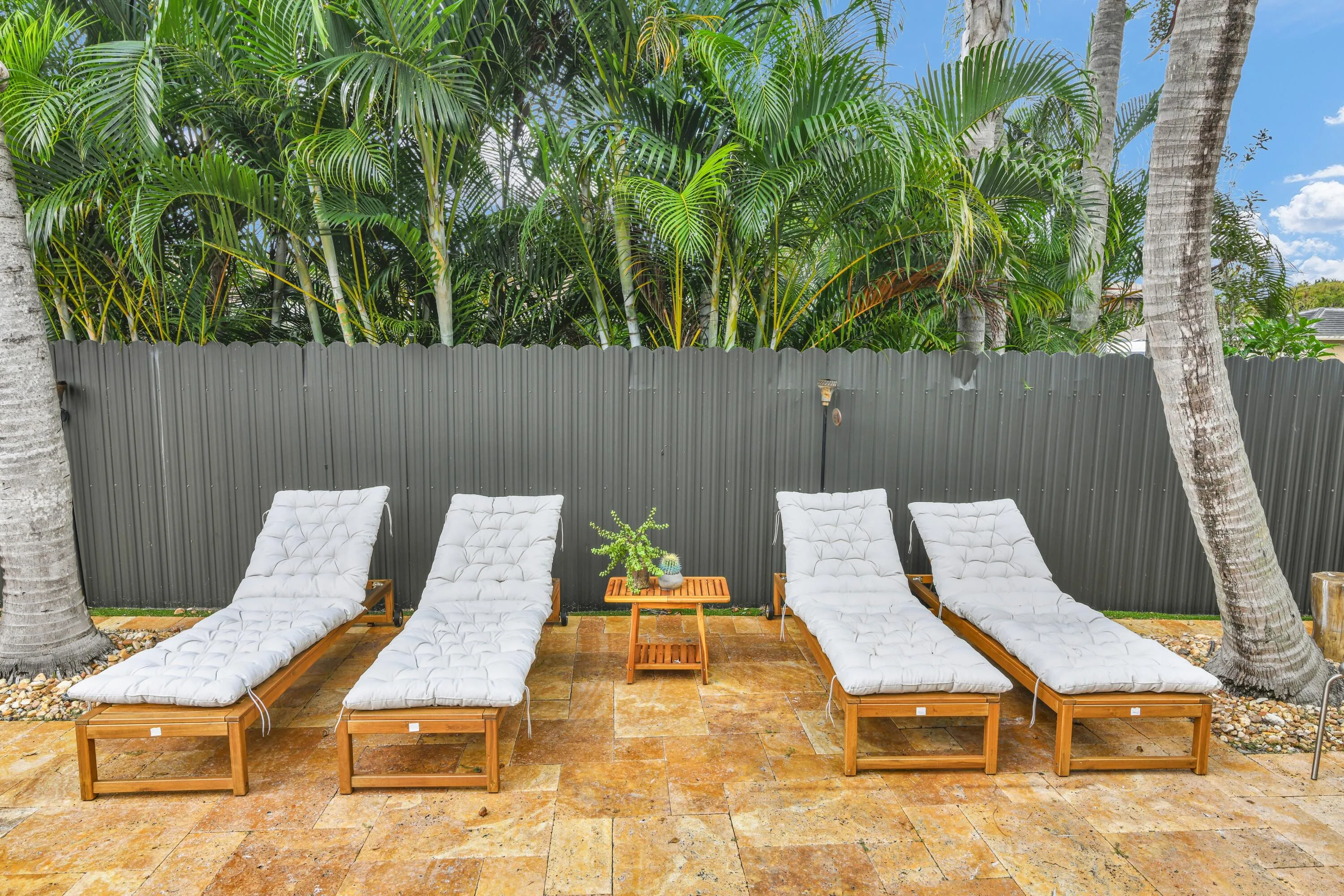Expansive outdoor patio with natural stone pavers, bordered by a solid privacy fence and lush tropical landscaping