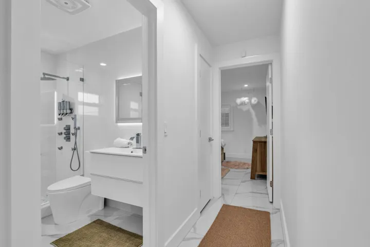 Bathroom featuring a wall-mounted vanity, illuminated mirror, walk-in shower with glass enclosure, rain shower head, and wall-mounted shower system