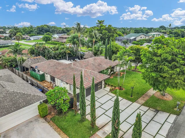 Property exterior featuring a tile roof, mature landscaping, a rectangular paver driveway, and a spacious green lawn