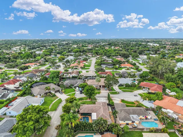 Aerial perspective showcasing a residential neighborhood with mature landscaping and multiple properties featuring private swimming pools