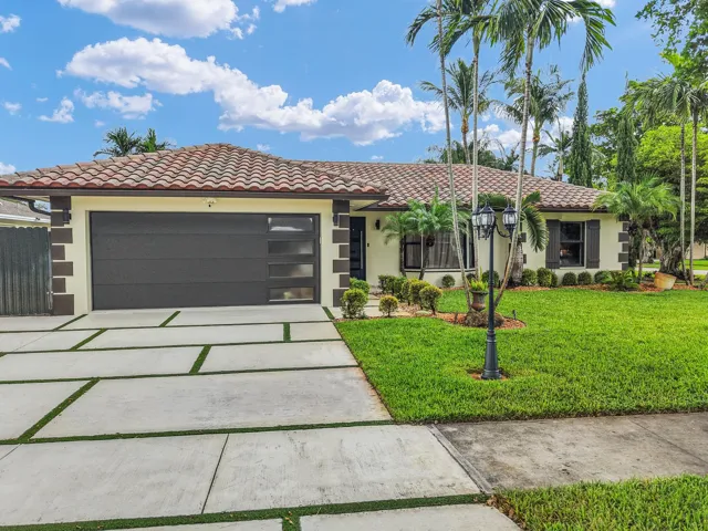 Exterior featuring a tile roof, stucco finish, a contemporary garage door with frosted panels, a concrete paver driveway with turf accents, and established landscaping