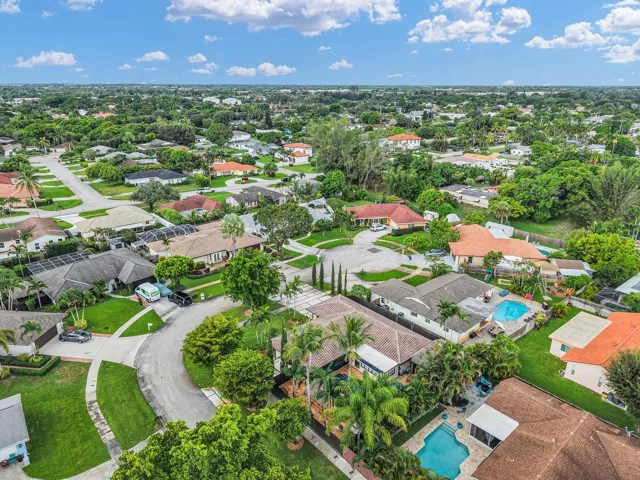 Residential neighborhood with mature trees, paved streets, and multiple properties featuring private swimming pools