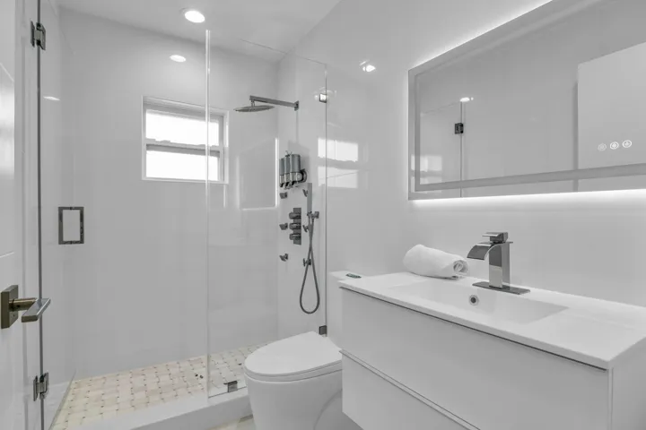 Glass-enclosed shower with a rainfall showerhead, white wall tiles, and a window