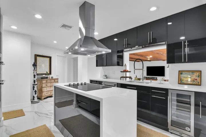 Kitchen featuring a center island cooktop, stainless steel range hood, white countertops, black cabinetry, and a built-in beverage cooler