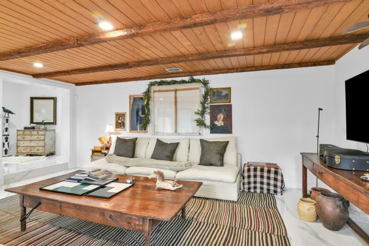 Recessed lighting, wood-finish ceiling, exposed wood beams, white walls, and a large window