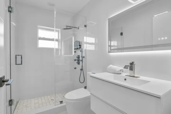 Modern bathroom featuring a frameless glass shower enclosure, a wall-mounted vanity with an integrated sink, an illuminated mirror, a waterfall faucet, and a wall-mounted toilet
