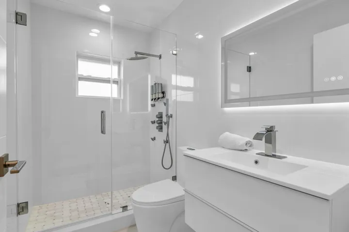Modern bathroom featuring a frameless glass shower enclosure, a wall-mounted vanity with integrated sink, and an illuminated mirrored medicine cabinet