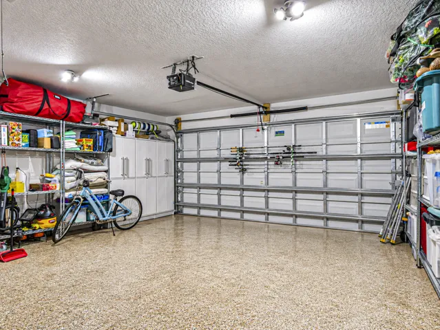 Garage space featuring a speckled epoxy floor, built-in white cabinetry, metal shelving units.
