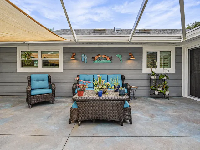Expansive patio area featuring a patterned concrete surface, horizontal siding, and a shade sail