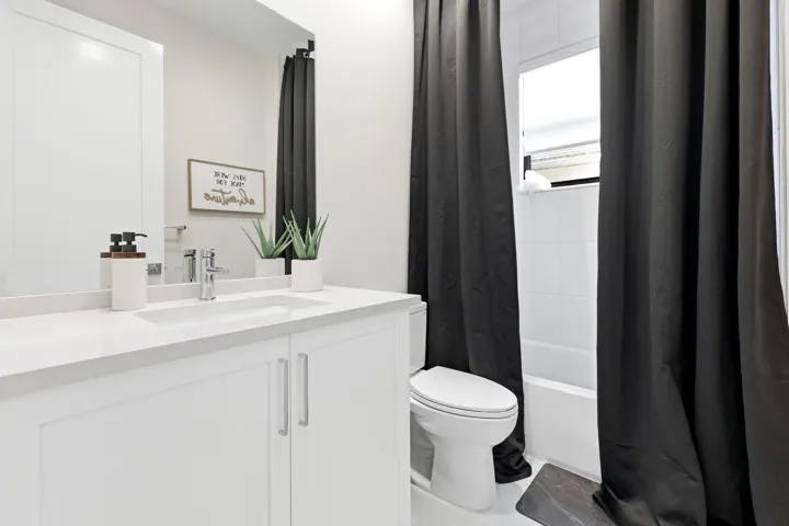 White vanity with integrated sink, chrome faucet, white countertop, white toilet, and white tiled shower surround