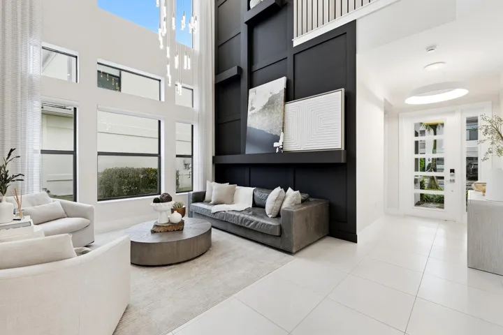 Two-story living area with expansive windows, a sleek black accent wall, and a contemporary chandelier