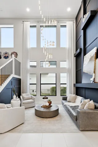 Two-story living area featuring a multi-pane window wall, suspended light fixture, tiled flooring, and a built-in dark accent wall with shelving
