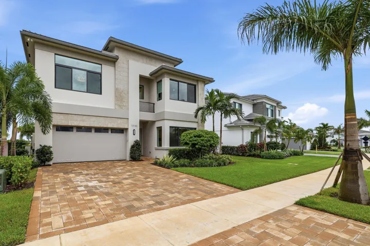 Modern architectural exterior with a stucco and stone facade, two-car garage, paver driveway, and mature landscaping