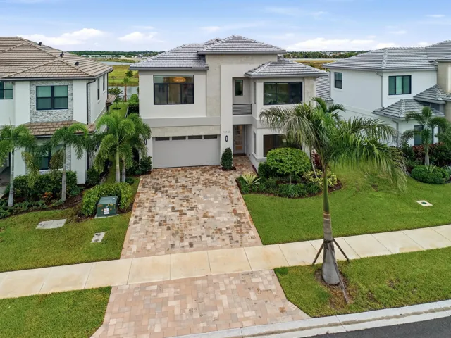 Modern stucco exterior with decorative stone accents, a paver driveway, and a tile roof