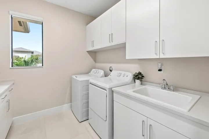 White shaker-style cabinetry with chrome hardware, an integrated laundry sink, light-toned countertop, and light-colored tile flooring