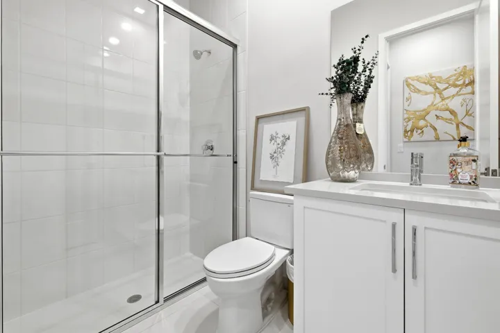 Shower with sliding glass doors, white tiled walls, white vanity with integrated sink, chrome faucet, and white cabinetry