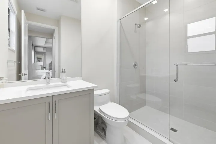 Contemporary bathroom featuring a single vanity with light grey cabinetry, a rectangular undermount sink, and a glass-enclosed shower with a chrome showerhead