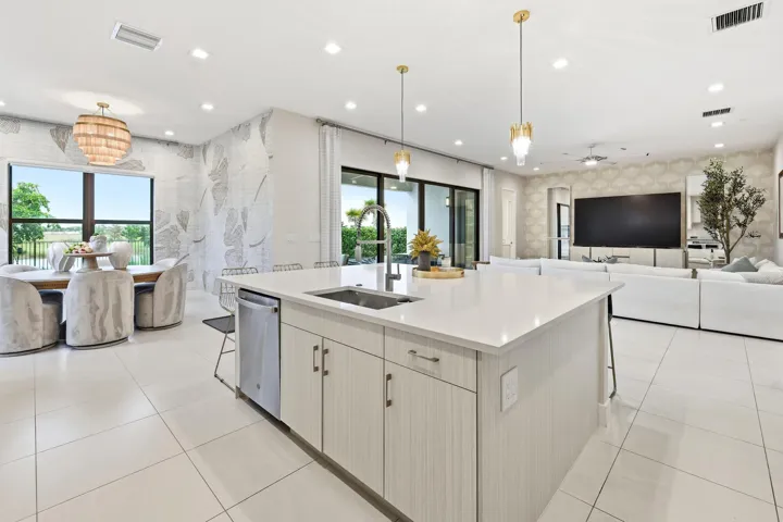 Open-concept interior featuring large format tile flooring, a kitchen island with sink and integrated dishwasher, and a dining area with expansive windows