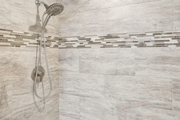 Shower featuring a multi-function shower head, brushed nickel fixtures, and a decorative mosaic tile accent band