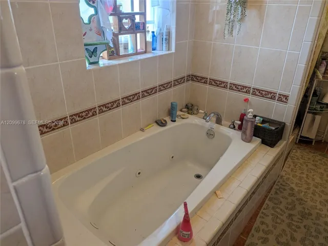 Jetted soaking tub featuring a tile surround, decorative accent border, and chrome plumbing fixtures