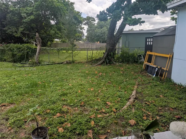 Backyard featuring a chain-link fence perimeter, mature trees, and an attached storage structure