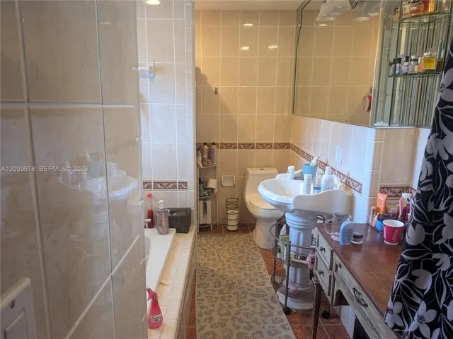 Full-tile bathroom featuring a porcelain pedestal sink, large soaking tub, wall-to-wall vanity mirror, and decorative tile trim