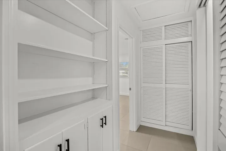 Built-in shelving with adjustable shelves, lower cabinetry with black hardware, louvered bi-fold doors, louvered sliding doors, and neutral floor tile