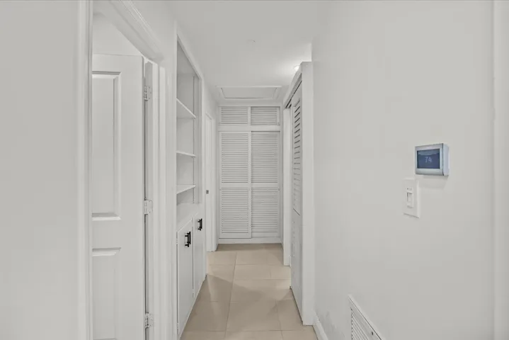 Hallway featuring built-in shelving, white paneled doors, louvered closet doors, and tile flooring