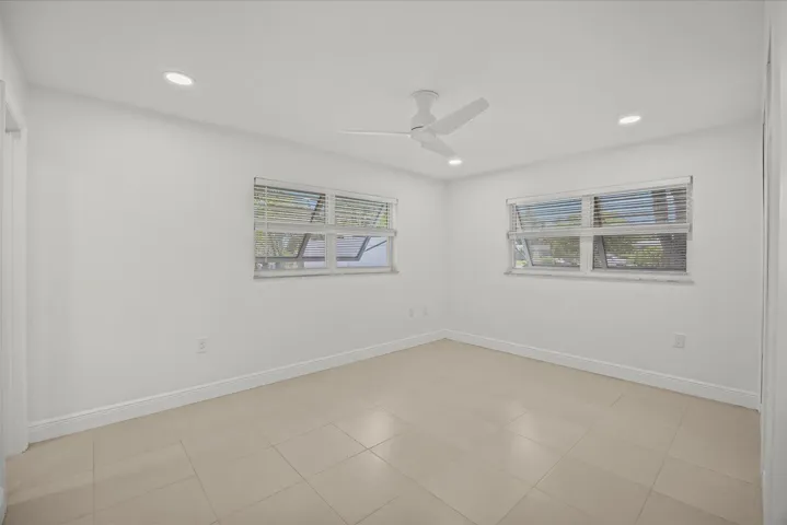 Neutral tone ceramic tile flooring, clean white walls, two windows with blinds, recessed lighting, and a ceiling fan