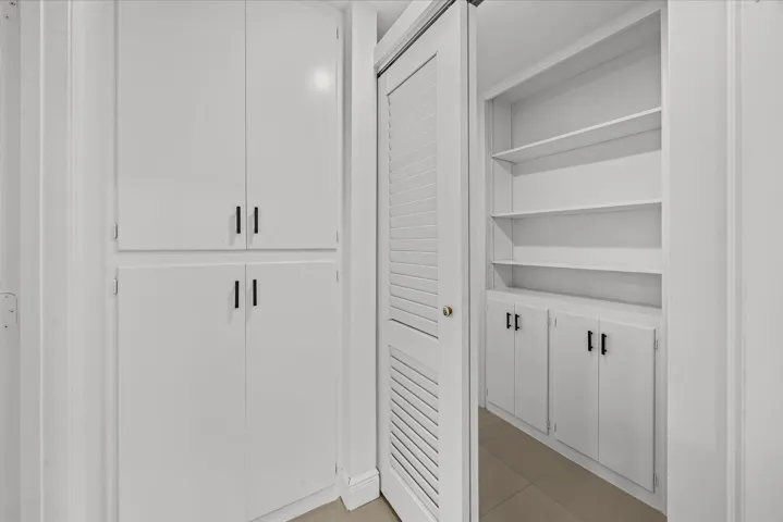 Built-in white cabinetry with black hardware, louvered closet door, and integrated shelving