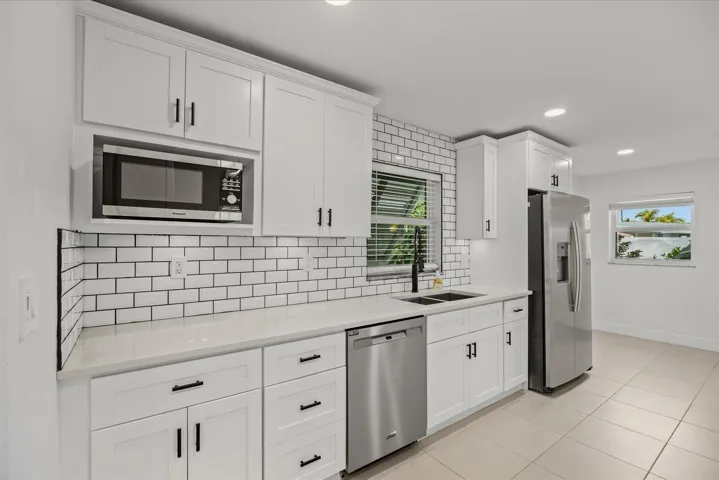 Modern kitchen featuring white shaker-style cabinetry, white subway tile backsplash with contrasting grout, stainless steel appliances including a microwave and dishwasher, quartz countertops, and tile flooring throughout the open layout
