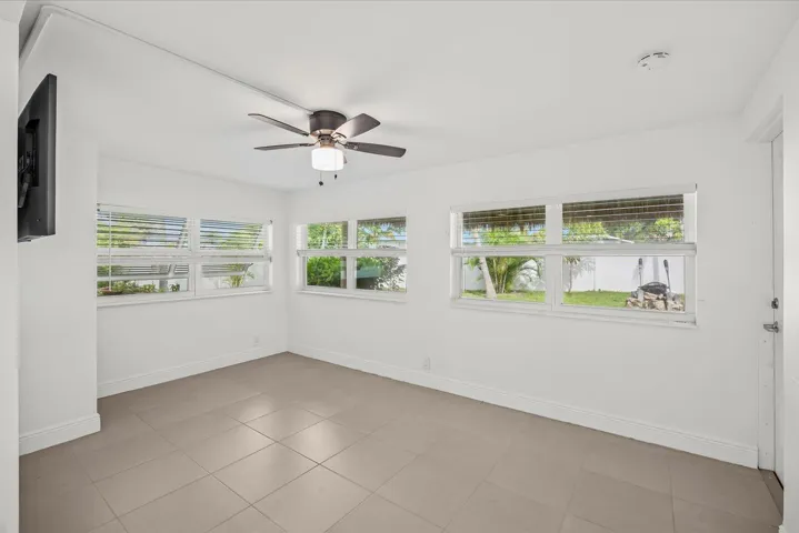White walls with multiple windows, a ceiling fan, and tiled flooring