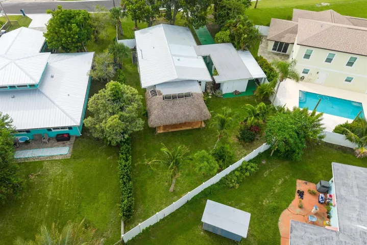 Aerial view showcasing expansive manicured grounds with mature landscaping, multiple white metal-roof structures, a resort-style swimming pool with surrounding hardscape, and generous green space ideal for outdoor living and recreation