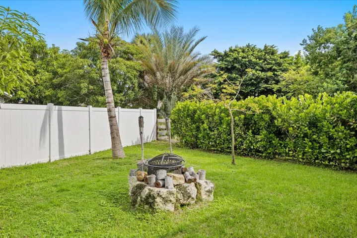 Green lawn area featuring a stone fire pit, a mature palm tree, and a white privacy fence