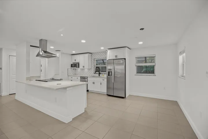 Kitchen featuring a large island with cooktop, stainless steel range hood, subway tile backsplash, white cabinetry, and tile flooring