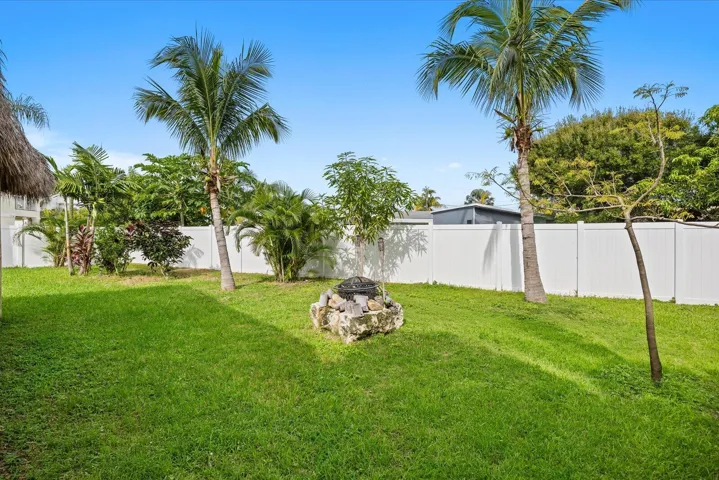 Expansive lawn with a built-in stone fire pit, mature palm trees, and a white privacy fence