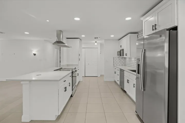 Kitchen featuring a large center island with a light-toned countertop, white cabinetry with dark hardware, stainless steel appliances, and subway tile backsplash