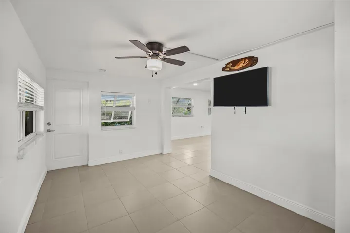 Light-toned tile flooring, white walls, multiple windows, a ceiling fan, and an arched entryway